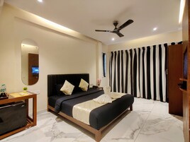 A modern hotel room with a bed, a desk, a mirror, a ceiling fan, and striped curtains.