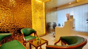 Een receptiebalie met een stenen muur, groene bekleden stoelen, en een raam met jaloezieën.