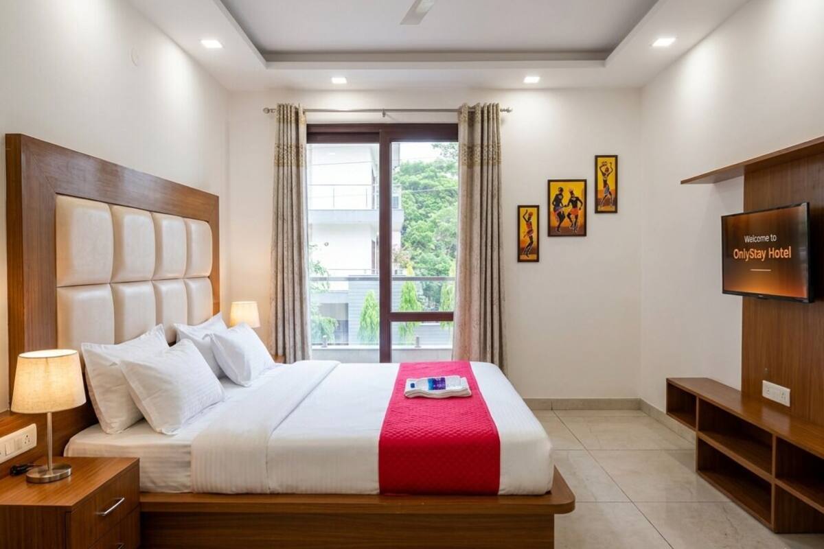 A hotel room with a bed, a TV, a nightstand, and a window with curtains.