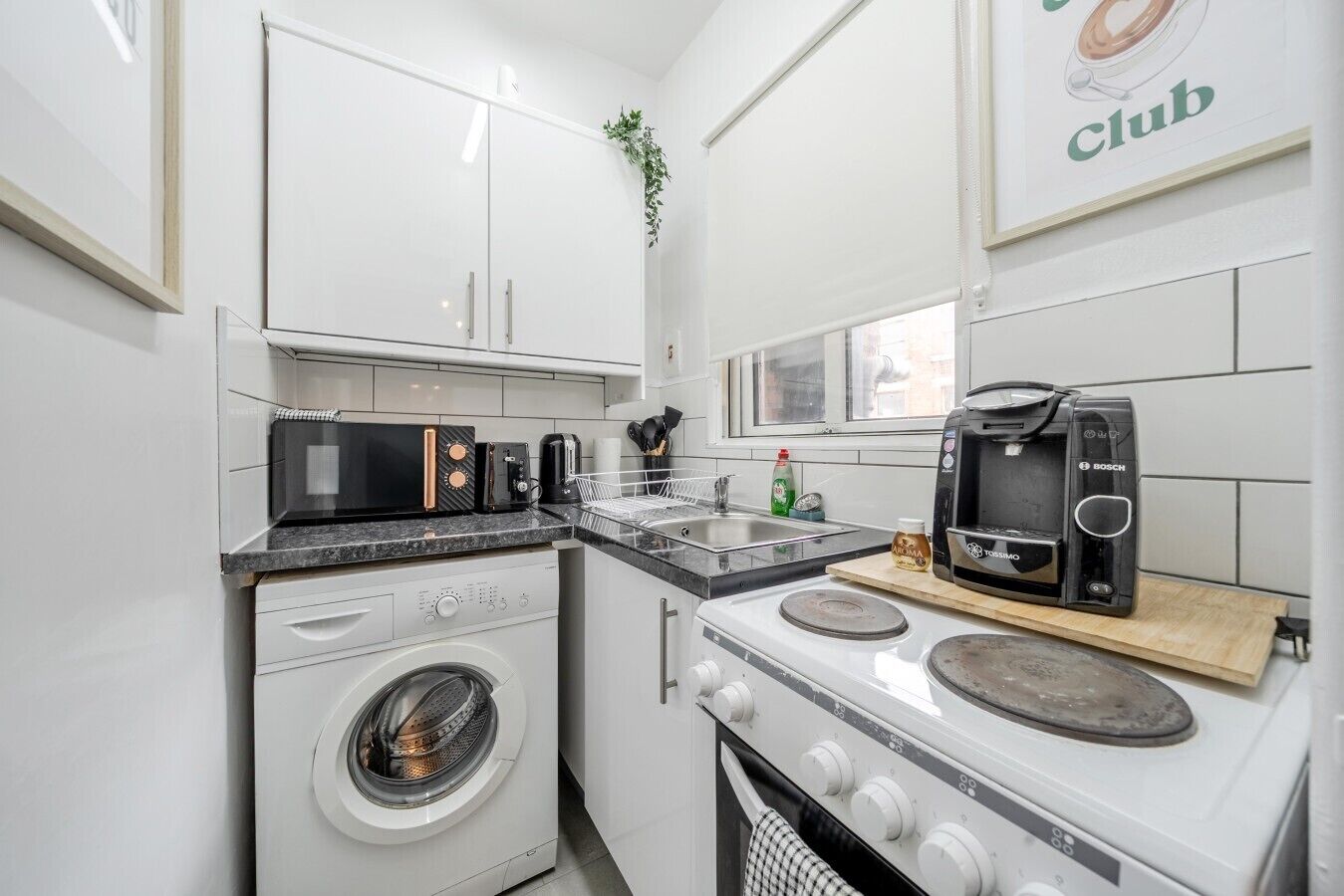 A compact kitchen with a washing machine, microwave, toaster, and coffee maker.
