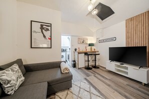 A modern living room with a sofa, a television, and a kitchen area in the background. - One-Bedroom Deluxe Apartment5 City Cent Manchester (Manchester)