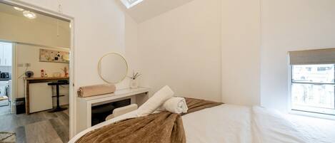 A bedroom with a bed, a bedside table, a mirror, and a window.