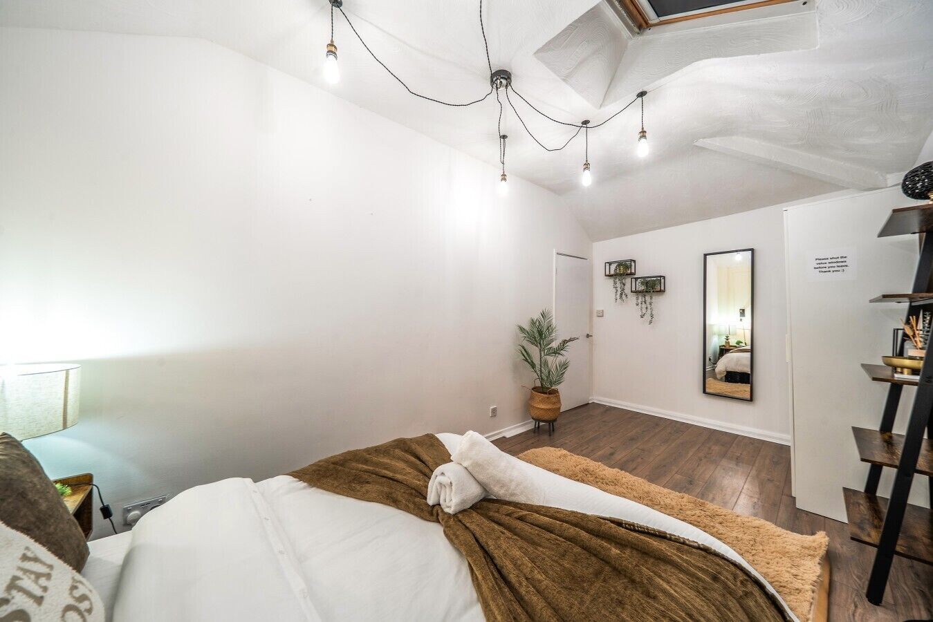 A bedroom with a bed, a potted plant, a mirror, and a shelf with items.