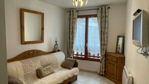 A living room with a sofa, a television, a cabinet, and a window with curtains. - VALBERG TOWN CENTRE - 3 rooms (50m2) 2 bedrooms + 36m2 terrace (VALBERG)