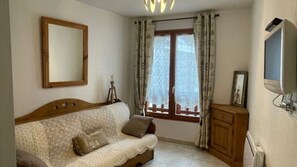 A living room with a sofa, a television, a cabinet, and a window with curtains. - VALBERG TOWN CENTRE - 3 rooms (50m2) 2 bedrooms + 36m2 terrace (VALBERG)