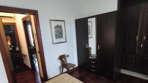 Un dormitorio con cama, una silla, un aparador y una puerta que da a otra habitación.