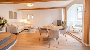A modern living room with a sofa, dining table, and chairs, wooden beams on the ceiling, and a large window. - Stylish vacation apartment at Kornmarkt | Limburg (Limburg)
