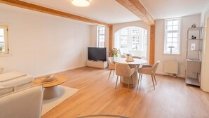 A modern living room with a flat-screen TV, a round dining table with chairs, a sofa, and a bookshelf. - Stylish vacation apartment at Kornmarkt | Limburg (Limburg)