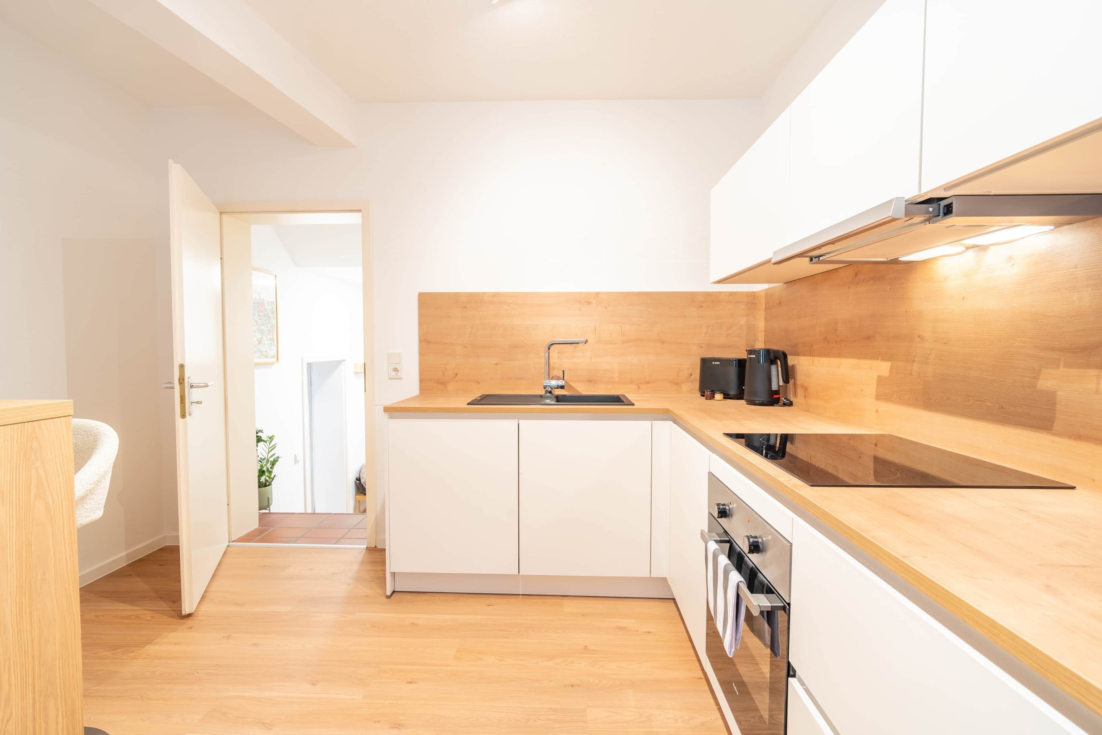 A modern kitchen with a wooden countertop, white cabinets, a built-in oven, and a sink.