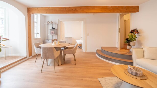 A modern living room with a wooden ceiling, a round dining table with chairs, a sofa, and a coffee table. - Stylish vacation apartment at Kornmarkt | Limburg (Limburg)