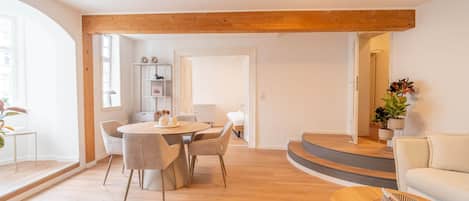 A modern living room with a wooden ceiling, a round dining table with chairs, a sofa, and a coffee table.