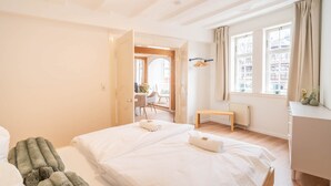 A hotel room with a large bed, a wooden bench, a desk, and a view of the city through the window. - Stylish vacation apartment at Kornmarkt | Limburg (Limburg)