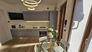 A modern kitchen with grey cabinets, a built-in oven, and a dining area with a glass table and chairs. - GREY1 (air conditioning and free private parking) (Verbania)