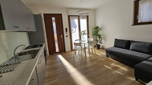 A modern kitchen with a built-in stove, a dining area with a table and chairs, and a dark-colored sofa in a living area. - GREY1 (air conditioning and free private parking) (Verbania)