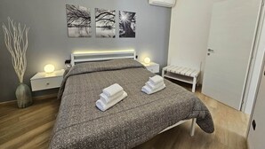 A modern bedroom with a large bed, bedside tables, a wall-mounted air conditioner, and a door. - GREY1 (air conditioning and free private parking) (Verbania)