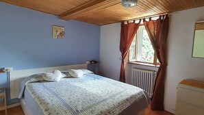 Ein Schlafzimmer mit Holzboden, einem Bett mit gemustertem Überwurf, einem Nachttisch, einer Kommode und einem Fenster mit Vorhängen.