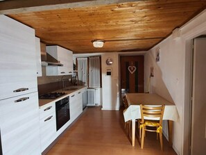 A kitchen with wooden ceiling, white cabinets, a dining table with chairs, and a radiator.