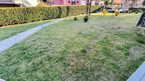 Zona residencial con césped cuidado, seto y un sendero que lleva a un edificio de fachada roja.