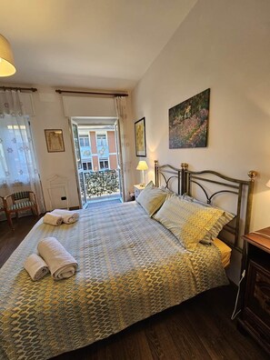 A bedroom with a bed, a chair, a bedside table, a window with curtains, and a painting on the wall. - Luna apartment (free parking & air conditioning) (Verbania)