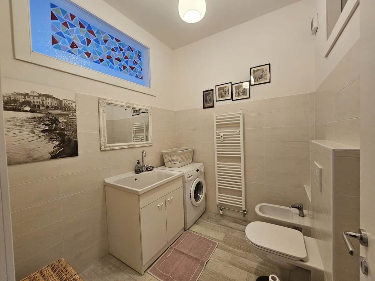 A compact bathroom with a washing machine, a sink, a toilet, and a towel rack.