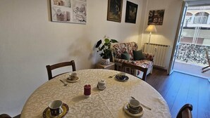 Ein Essbereich mit einem runden Tisch, der für Tee gedeckt ist, einer Couch mit einem floralen Kissen und Blick durch eine Glastür.