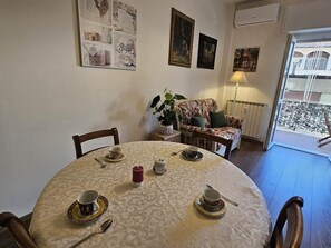 A dining area with a round table set for tea, a sofa with a floral cushion, and a view through a glass door. - Luna apartment (free parking & air conditioning) (Verbania)