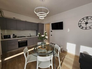 A modern kitchen with a dining area, a TV mounted on the wall, and a clock. - GREY 2 (air conditioning and free private parking) (Verbania)