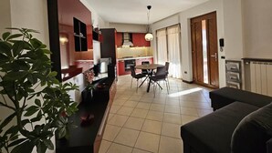Una sala de estar con sofá, un comedor con mesa y sillas, una cocina con armarios rojos y una planta en maceta.