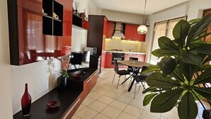 Una cocina moderna con armarios rojos, una zona de comedor con mesa y sillas, y una planta grande en primer plano.
