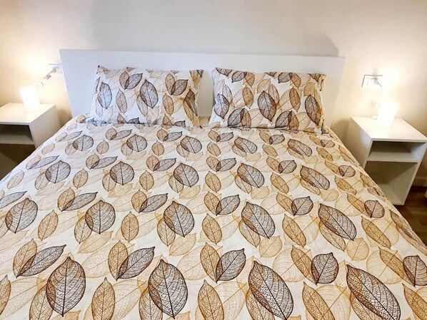 A bed with a leaf-patterned bedspread, two pillows, and bedside lamps on white nightstands. - MATILDE APARTMENT LAKE CENTER (Verbania)