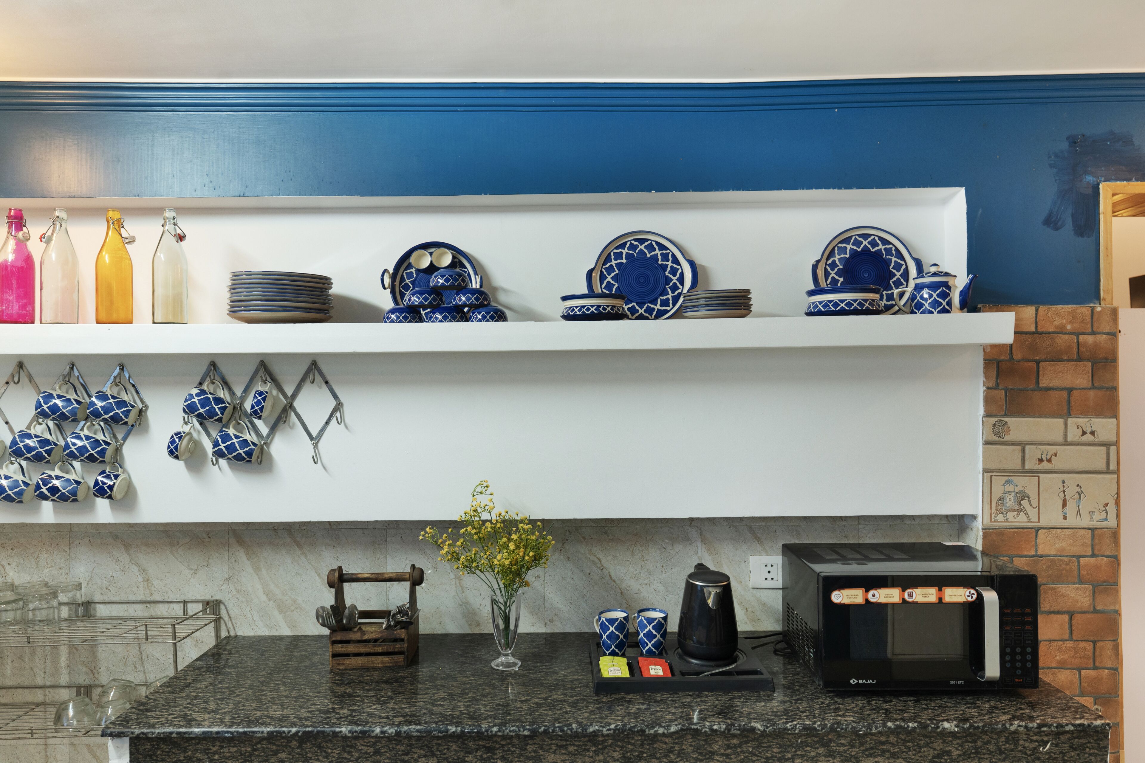Una cocina con microondas, cafetera y diferentes utensilios de cocina en estantes.
