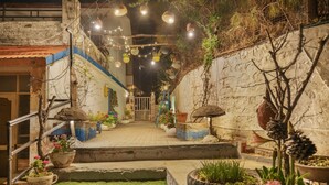 Un estrecho callejón con escaleras que conducen a una puerta, decorado con luces colgantes y plantas en macetas.