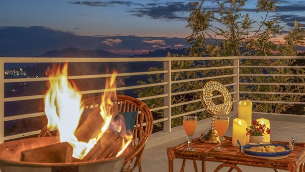 Un brasero con llamas, una mesa con bebidas y velas, y vistas del paisaje.