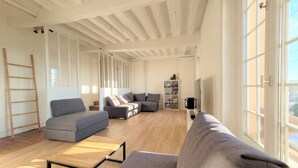 Un salón amplio con suelo de madera, un sofá gris, una mesa de centro y una estantería.