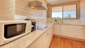 Una cocina con armarios blancos, microondas, estufa y ventana con vistas.