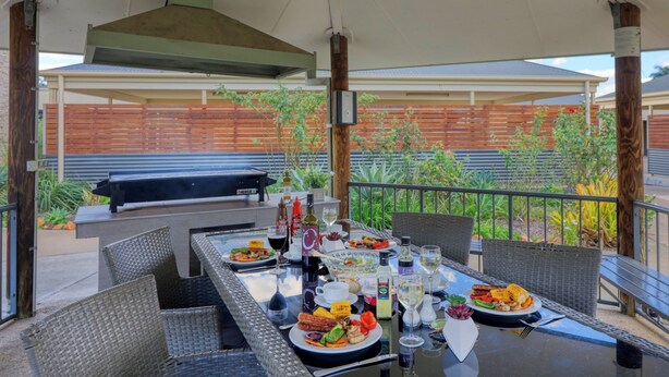 Un espacio al aire libre para comer con una parrilla, mesa, sillas y una variedad de comida y bebidas.