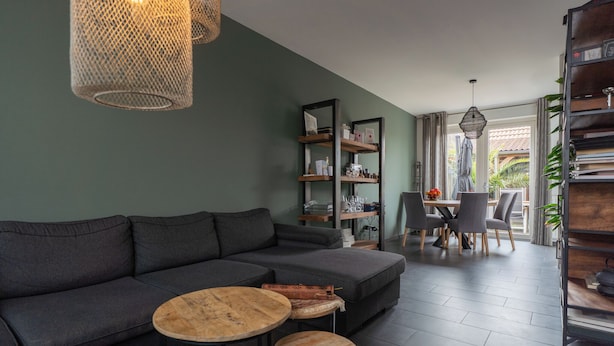 Un salon moderne avec un canapé d’angle, deux petites tables rondes et un coin repas avec des chaises.