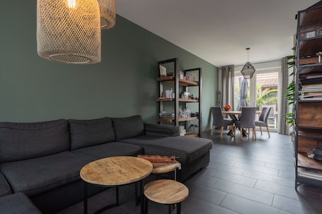 A modern living room with a sectional sofa, two small round tables, and a dining area with chairs.
