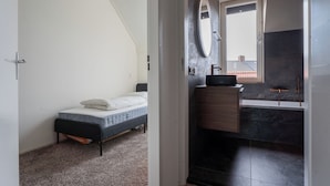 Une chambre avec un lit, une salle de bain avec un lavabo et un miroir, et une vue sur l  ’extérieur.