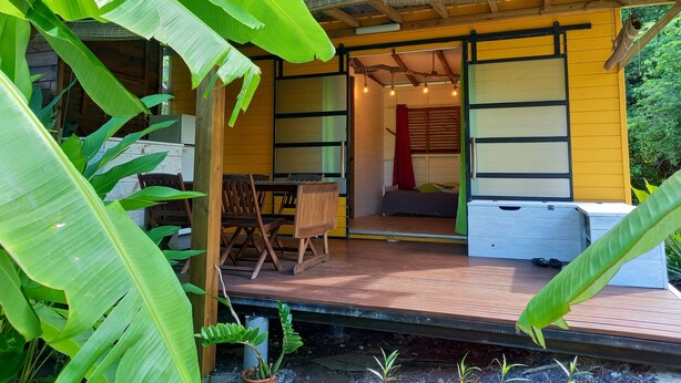 A wooden structure with a porch, a bed, and a table with chairs. - Charming Bungalow (Le Vauclin)