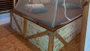 A rustic wooden bed with a mosquito net, a rolled towel, and a pillow. - Charming Bungalow (Le Vauclin)