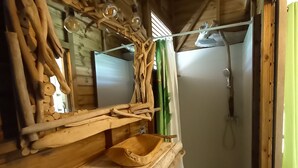 A rustic wooden bathroom with a wooden sink, a shower, and a hanging light fixture. - Charming Bungalow (Le Vauclin)
