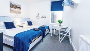 Une chambre d’hôtel moderne équipée de deux lits, d’un bureau, d’une chaise, d’une petite table, d’une plante en pot et d’une fenêtre donnant sur un paysage agréable.