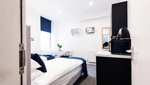 Une chambre d’hôtel équipée d’un lit, d’un bureau avec un ordinateur, d’une télévision et d’une machine à café.
