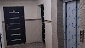 A hallway with a black door, a wall-mounted elevator, and a textured wall. - Rental per night in Tlemcen - imama Mansourah Appartement F4 neuf (Tlemcen)