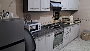 A kitchen with a gas stove, oven, and a microwave. There are cabinets, a sink, and a trash bin. - Rental per night in Tlemcen - imama Mansourah Appartement F4 neuf (Tlemcen)