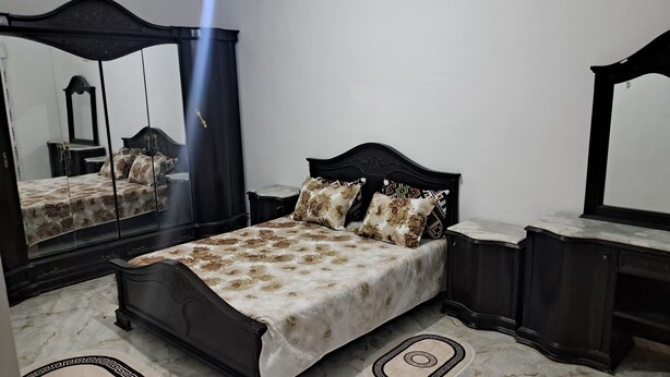 A bedroom with a bed, a nightstand, a dresser, a mirror, and a marble floor. - Rental per night in Tlemcen - imama Mansourah Appartement F4 neuf (Tlemcen)