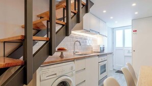 Et lille køkken med vaskemaskine, mikroovn og vask. En trætrappe med et moderne design.