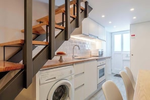 Eine kleine Küche mit Waschmaschine, Mikrowelle und einer Holztreppe.