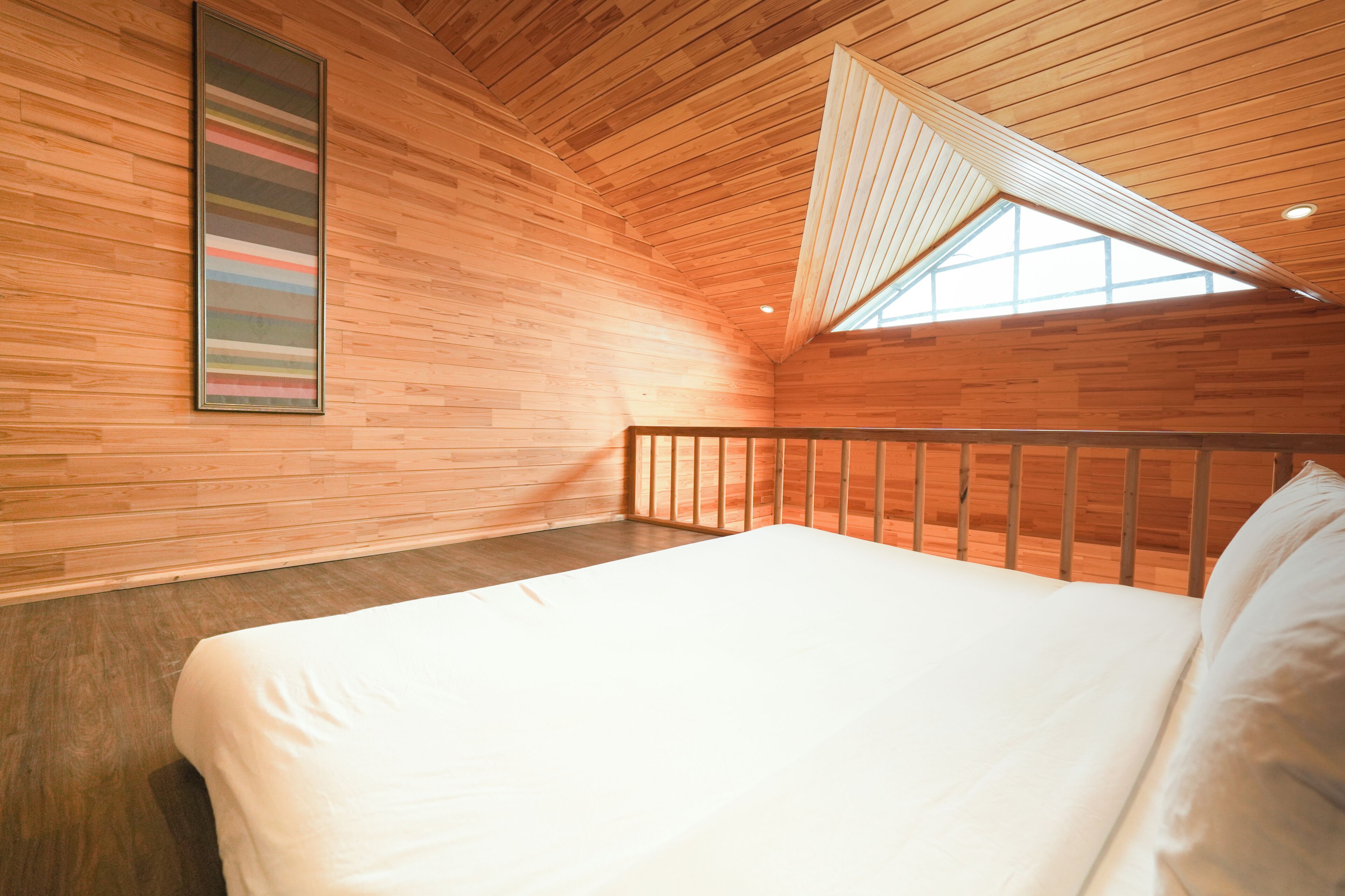 Une chambre avec un plafond en bois, un lit, une fenêtre et une œuvre d’art encadrée accrochée au mur.